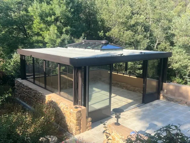Véranda aluminium à toit plat avec lanterneau, posée sur un mur en pierre